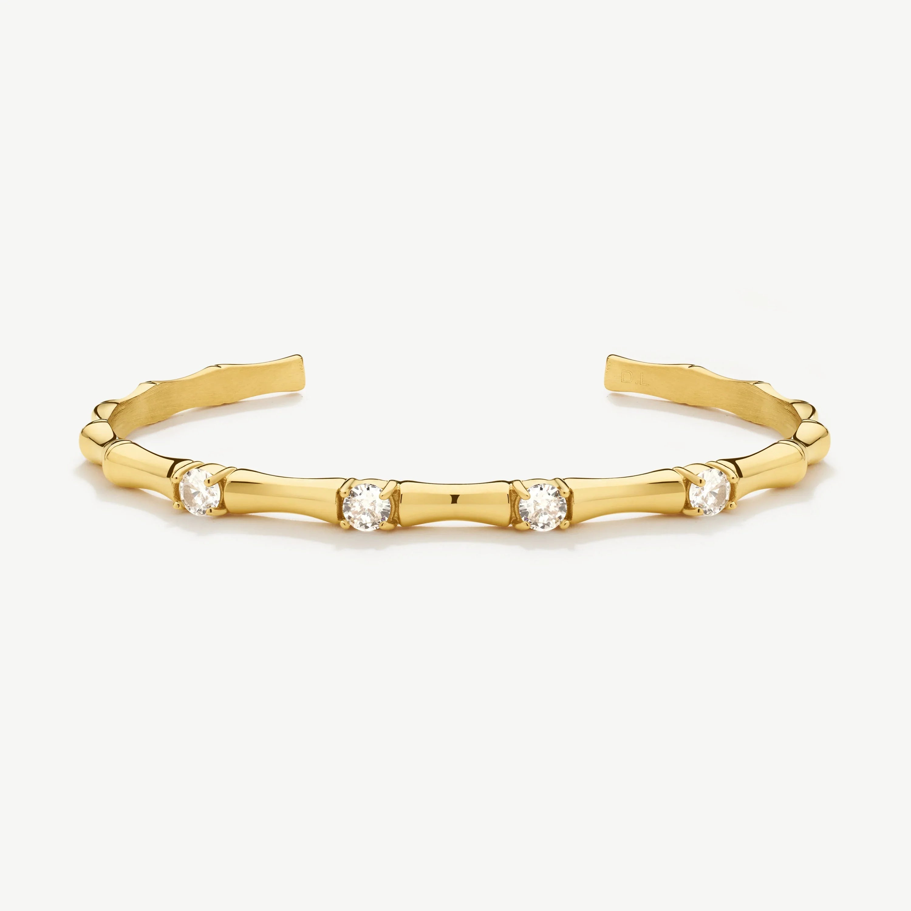 Gold cuff bracelet with bamboo-inspired design and four round clear gemstones on white background