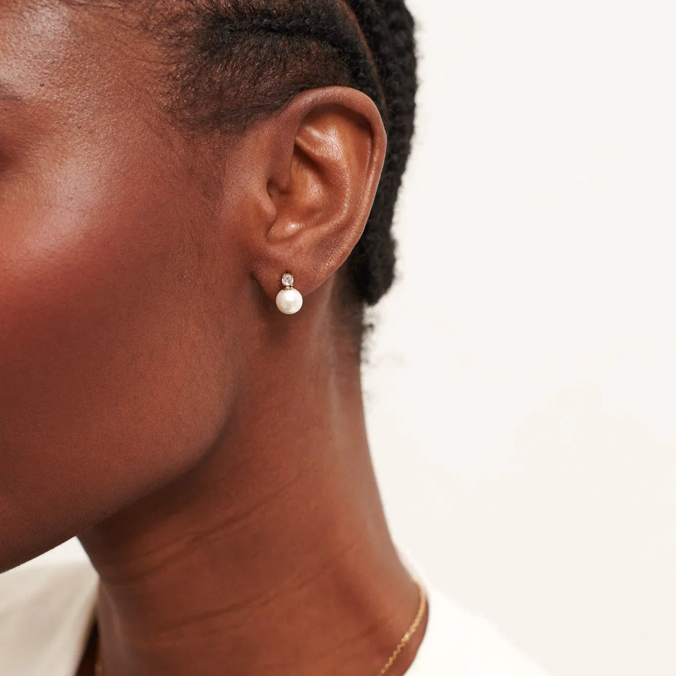 Close-up of woman wearing pearl stud earring with diamond detail on neutral background