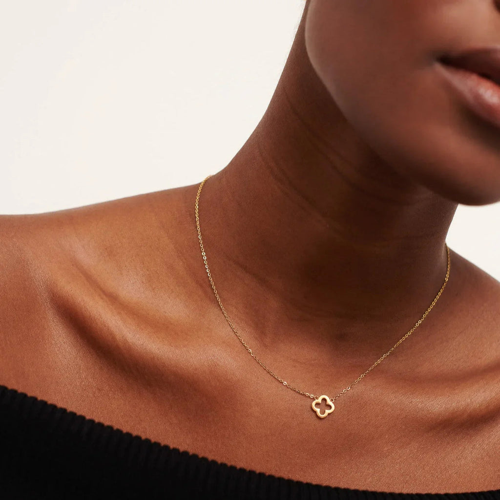 Close-up of a woman wearing a delicate gold clover pendant necklace on a fine chain with a black off-shoulder top