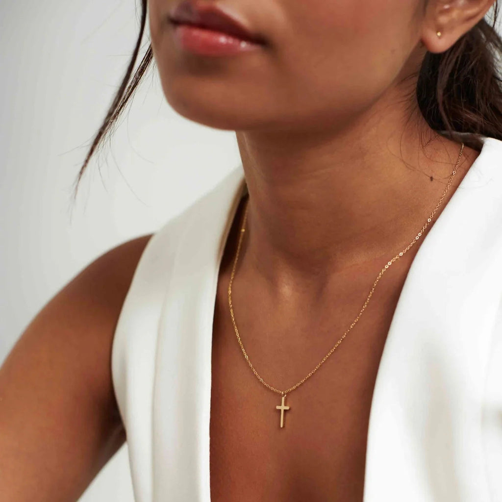 Close-up of woman wearing gold cross necklace with white sleeveless top on neutral background
