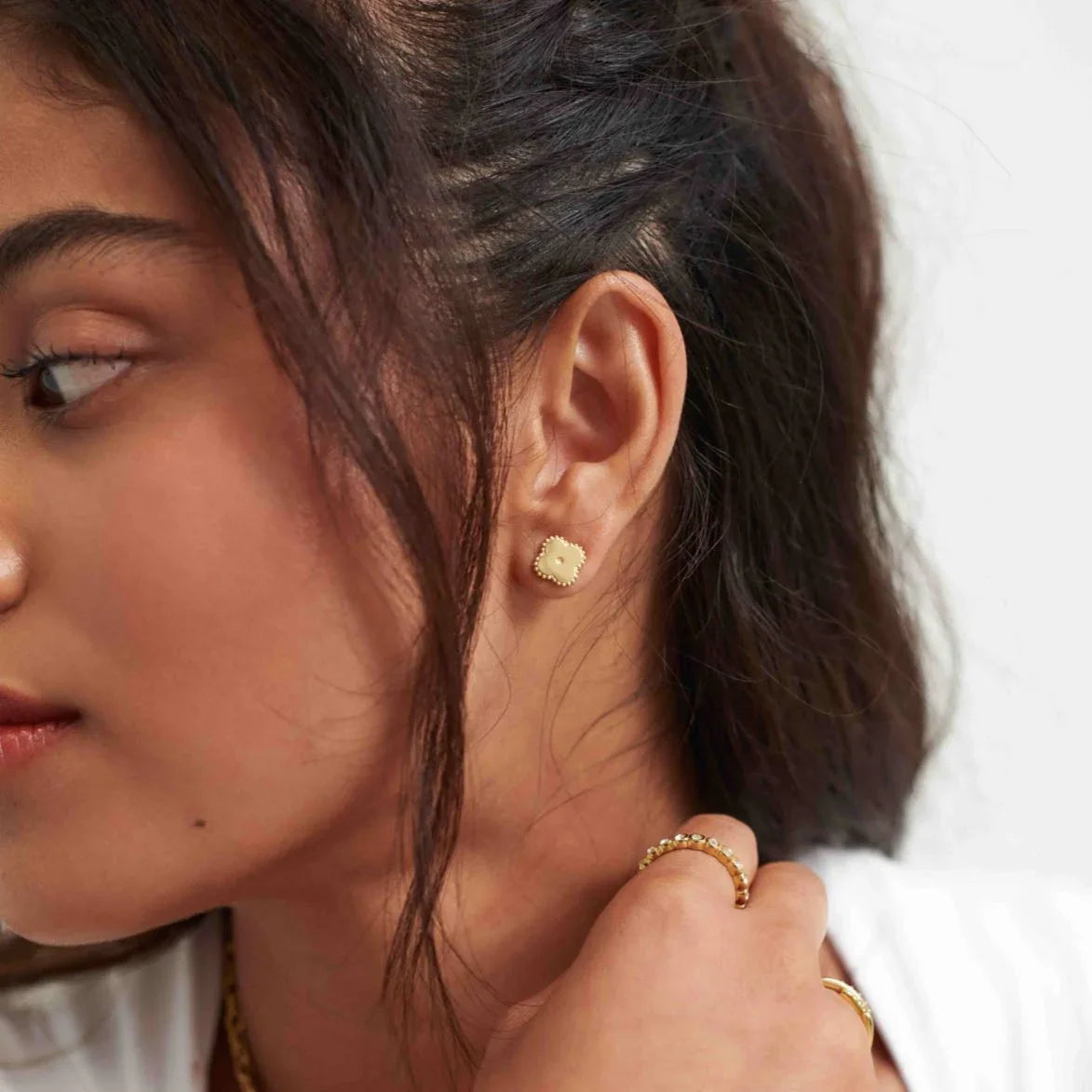 Close-up of woman wearing gold cluster stud earrings and gold rings with textured details