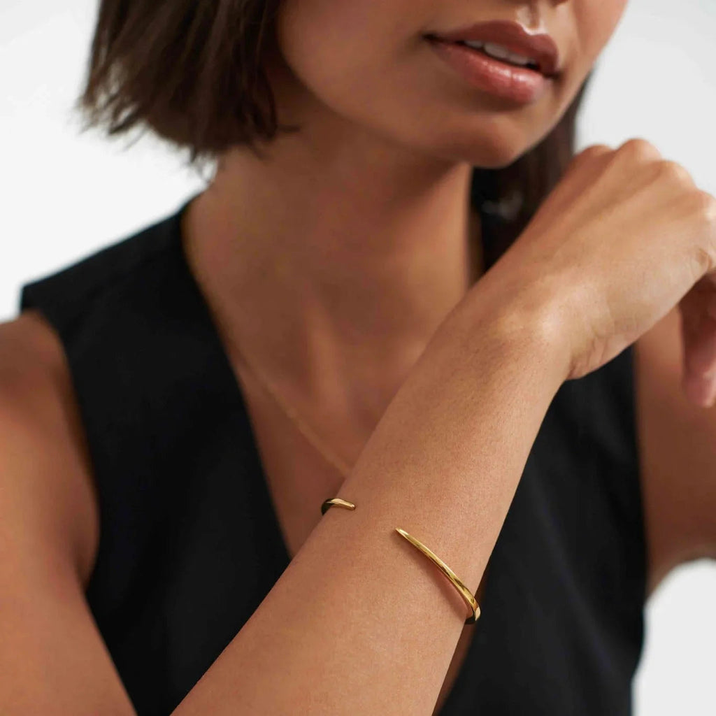 Close-up of woman wearing modern gold open cuff bracelet and black sleeveless top