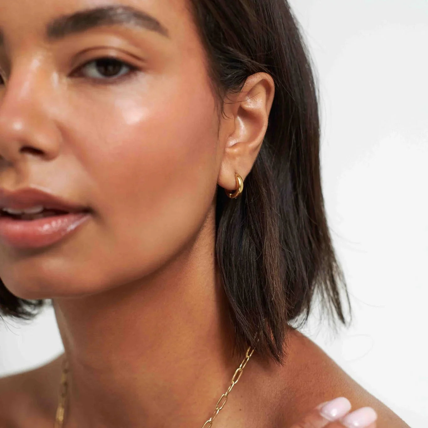 Close-up of woman with glowing skin wearing small gold hoop earring and chain necklace