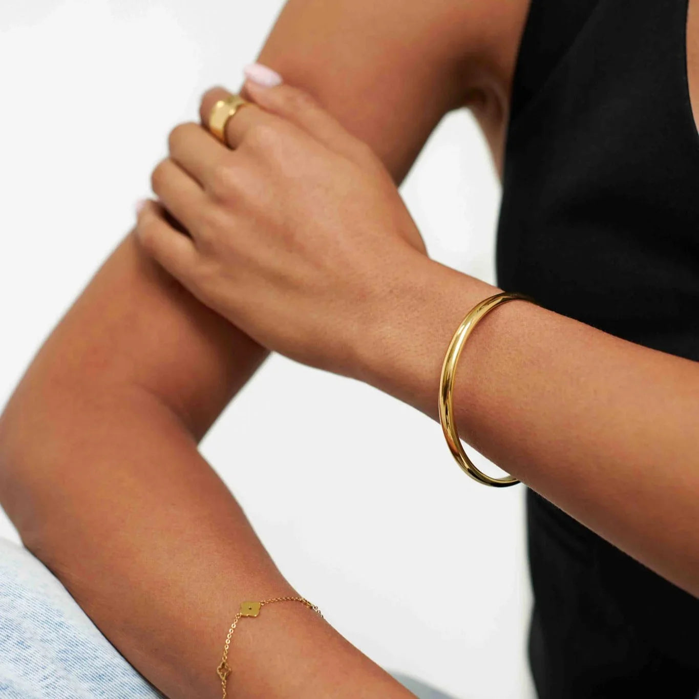 Close-up of woman wearing gold bangle, delicate gold chain bracelet, and gold ring on arm with black top