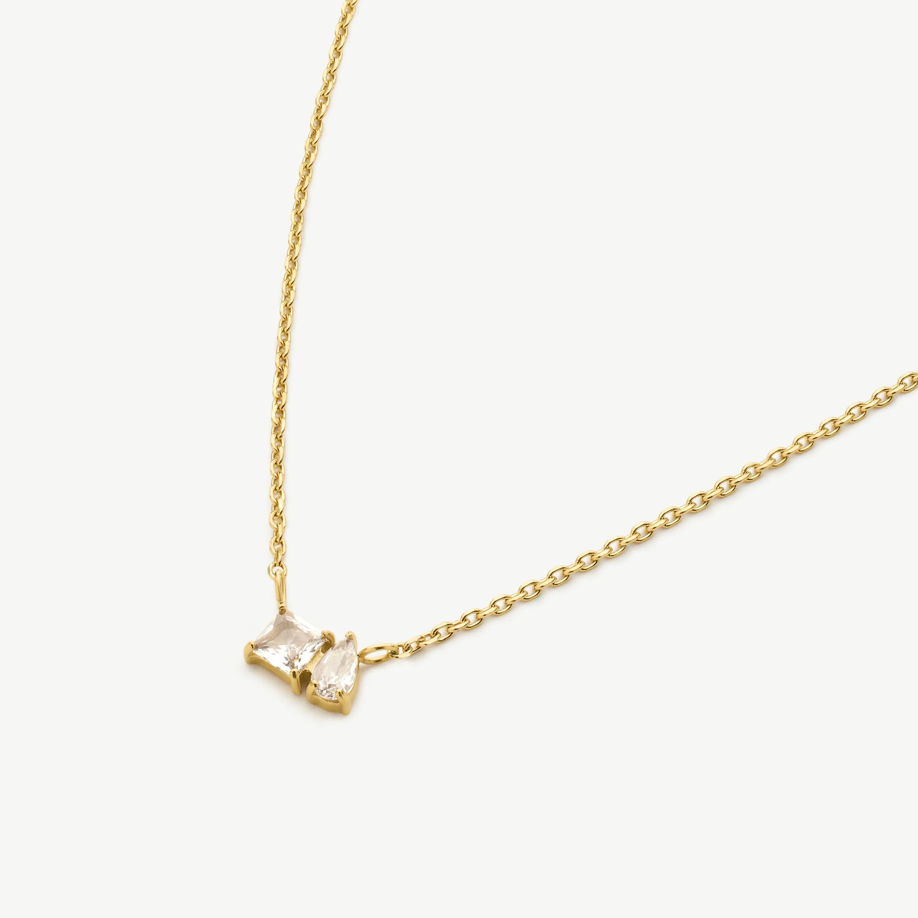 Gold chain necklace with square and teardrop clear gemstone pendants on white background