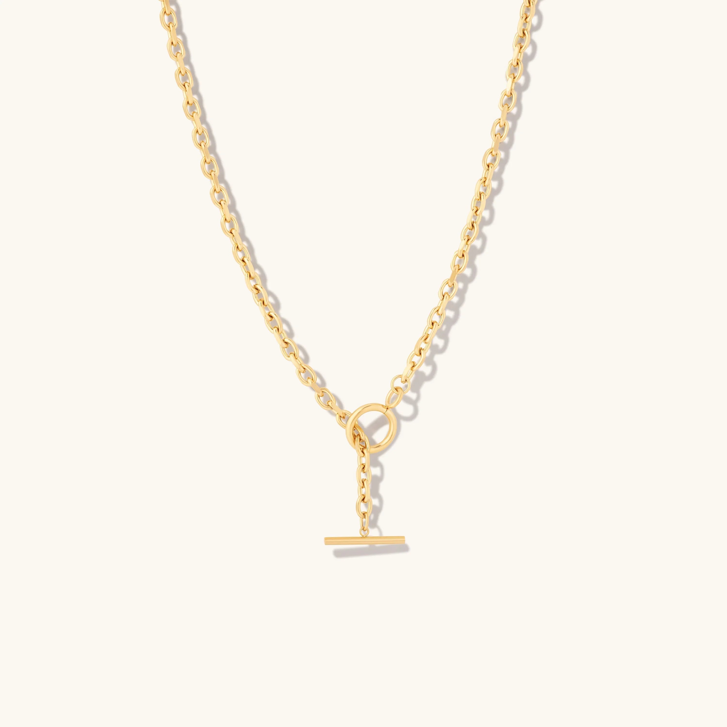 Gold chain necklace with toggle clasp on beige background
