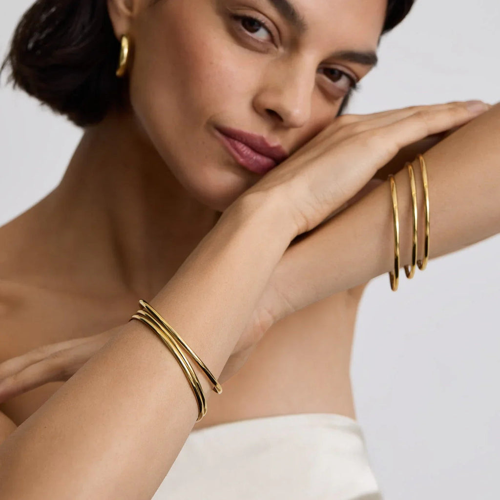 Woman wearing minimalist classic gold bangles and gold hoop earrings with a neutral background