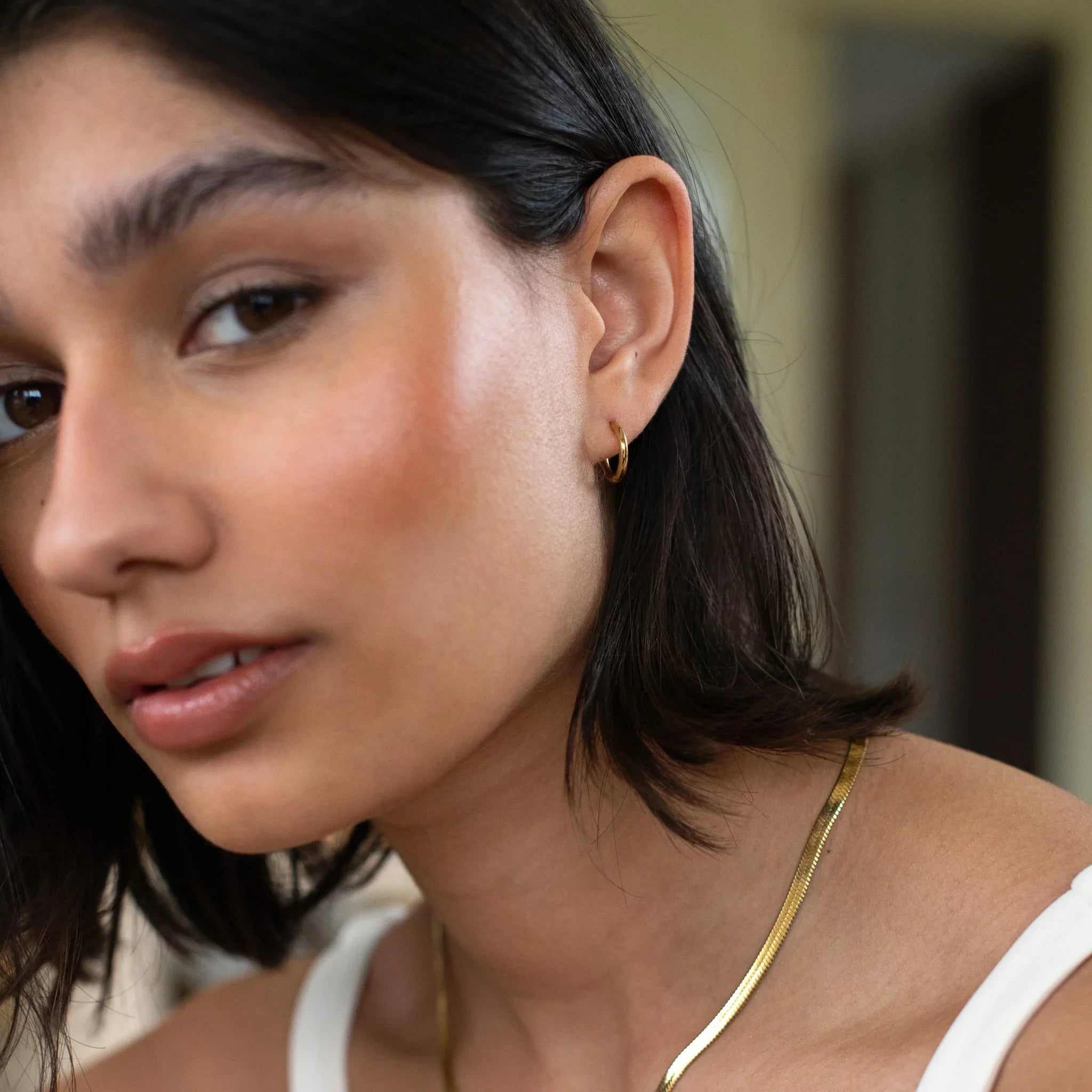 Close-up of a woman with short dark hair wearing a small gold hoop earring and gold necklace