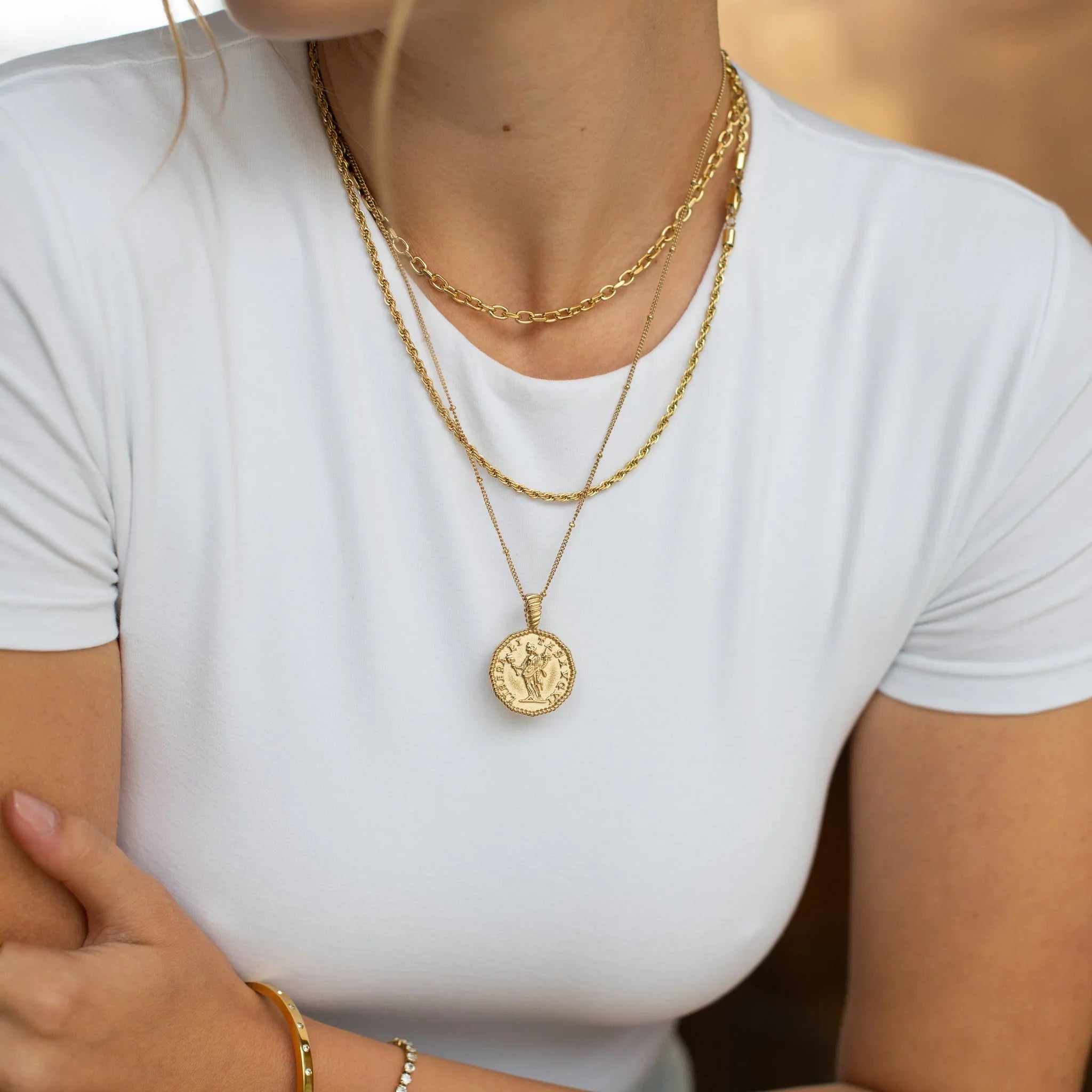 Close-up of woman in white shirt wearing layered gold chain necklaces and gold bracelets