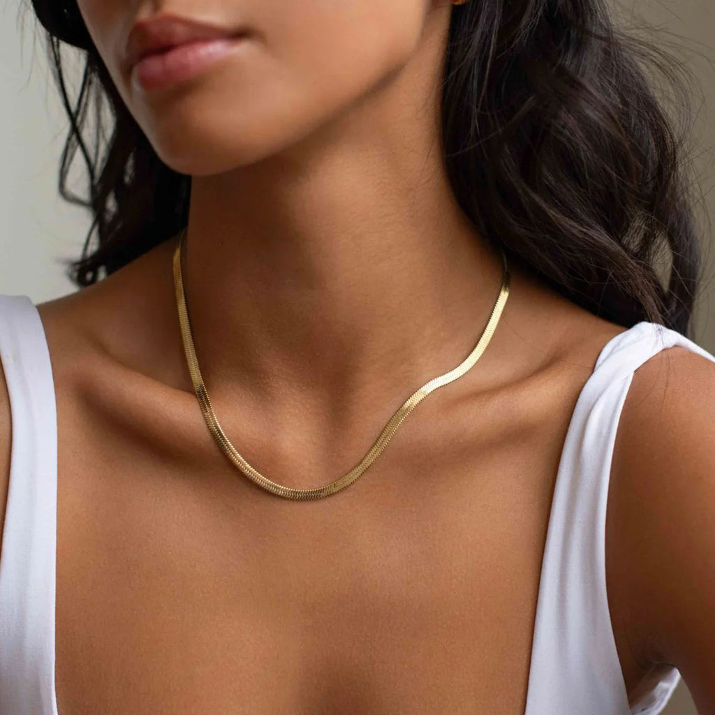 Close-up of woman wearing a simple gold chain necklace with white tank top and dark wavy hair