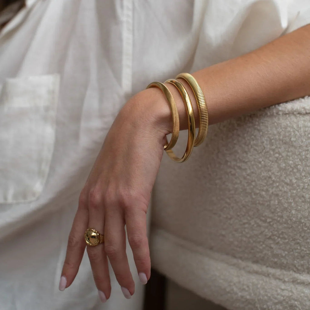 Woman's hand with gold bangles and a textured gold ring against white fabric and cozy background