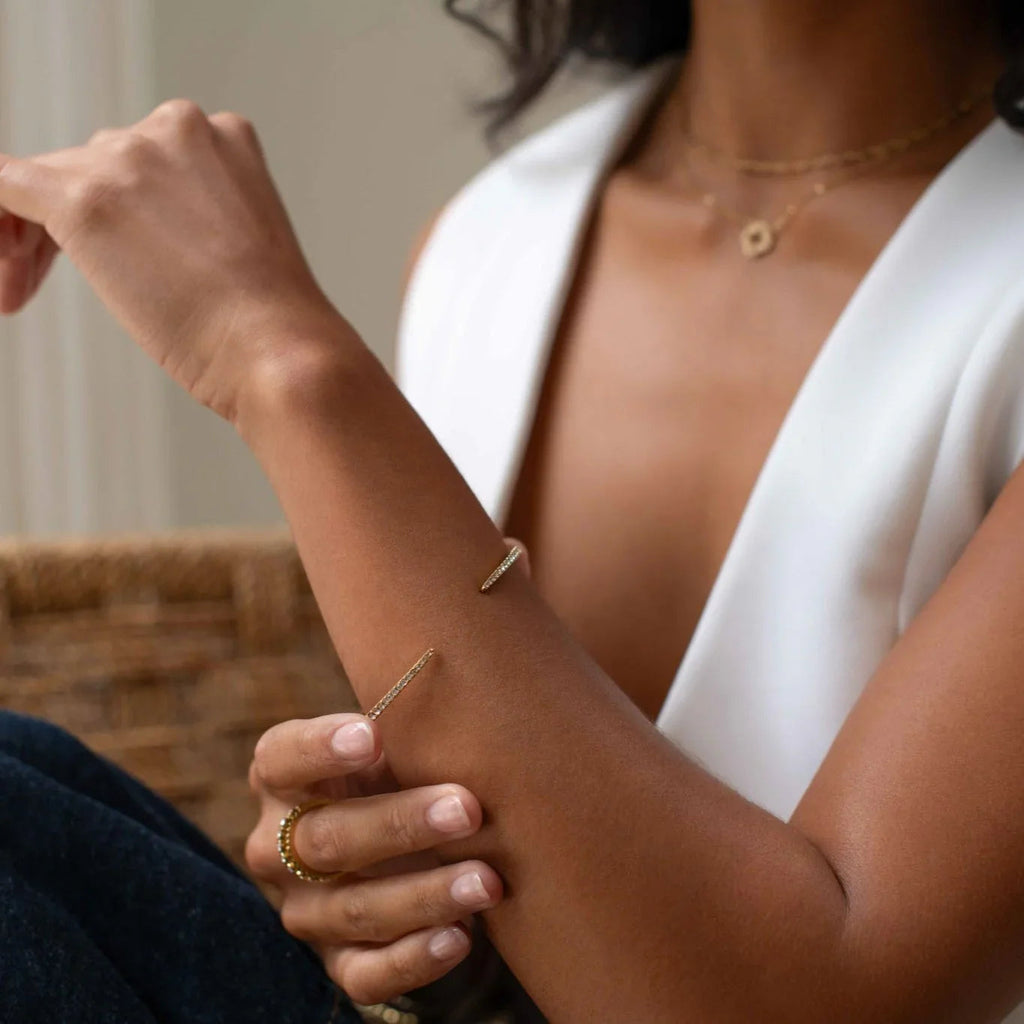 Close-up of woman wearing gold open cuff bracelet, gold ring, and layered gold necklaces with white sleeveless top