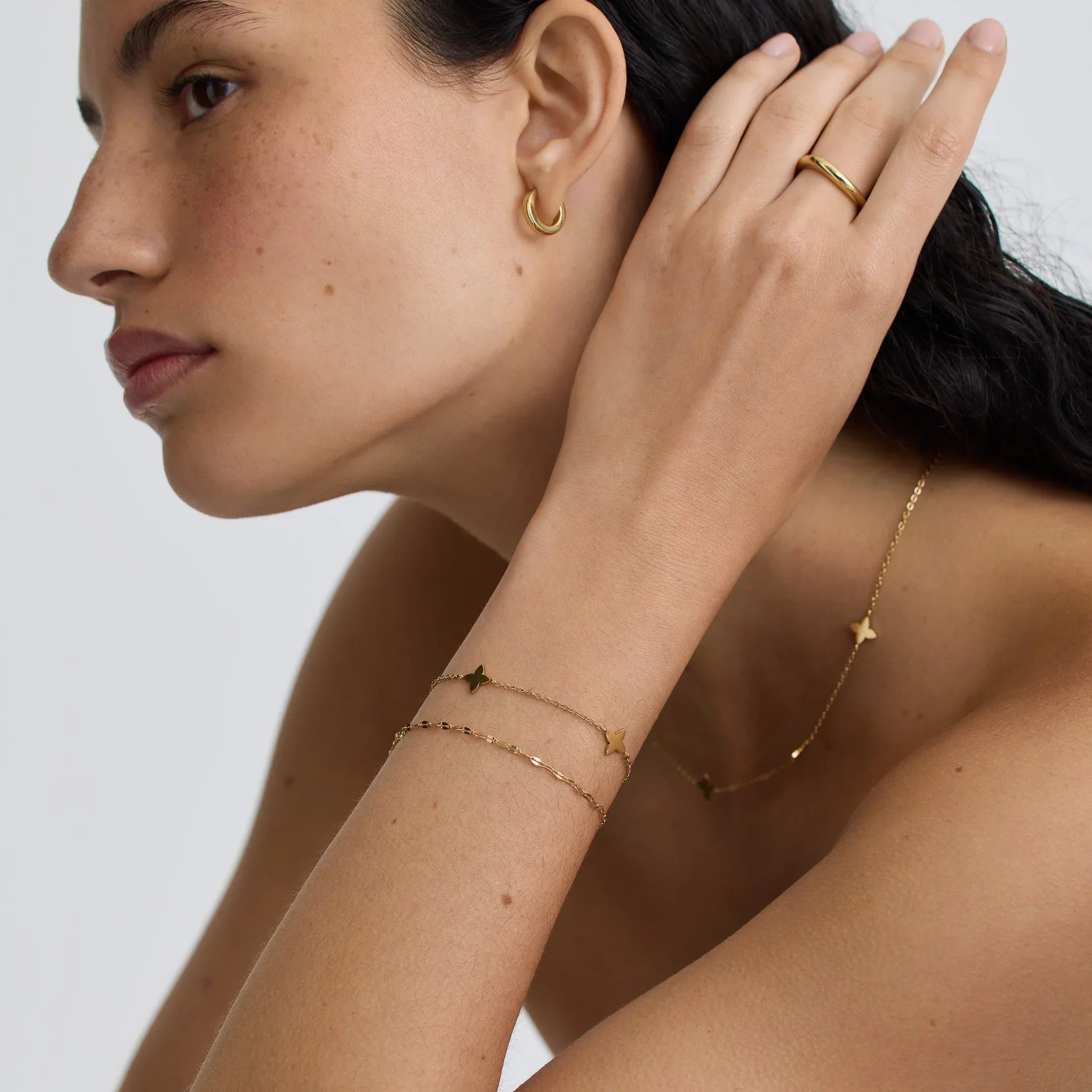 Close-up of woman wearing gold hoop earrings, gold dainty bracelets, ring, and necklace with butterfly charms