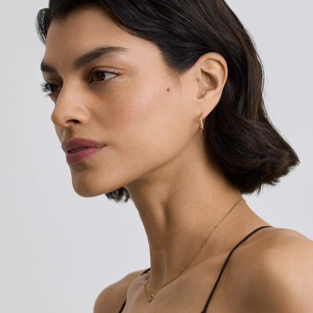 Profile of woman wearing small gold hoop earrings and delicate gold necklace on a white background