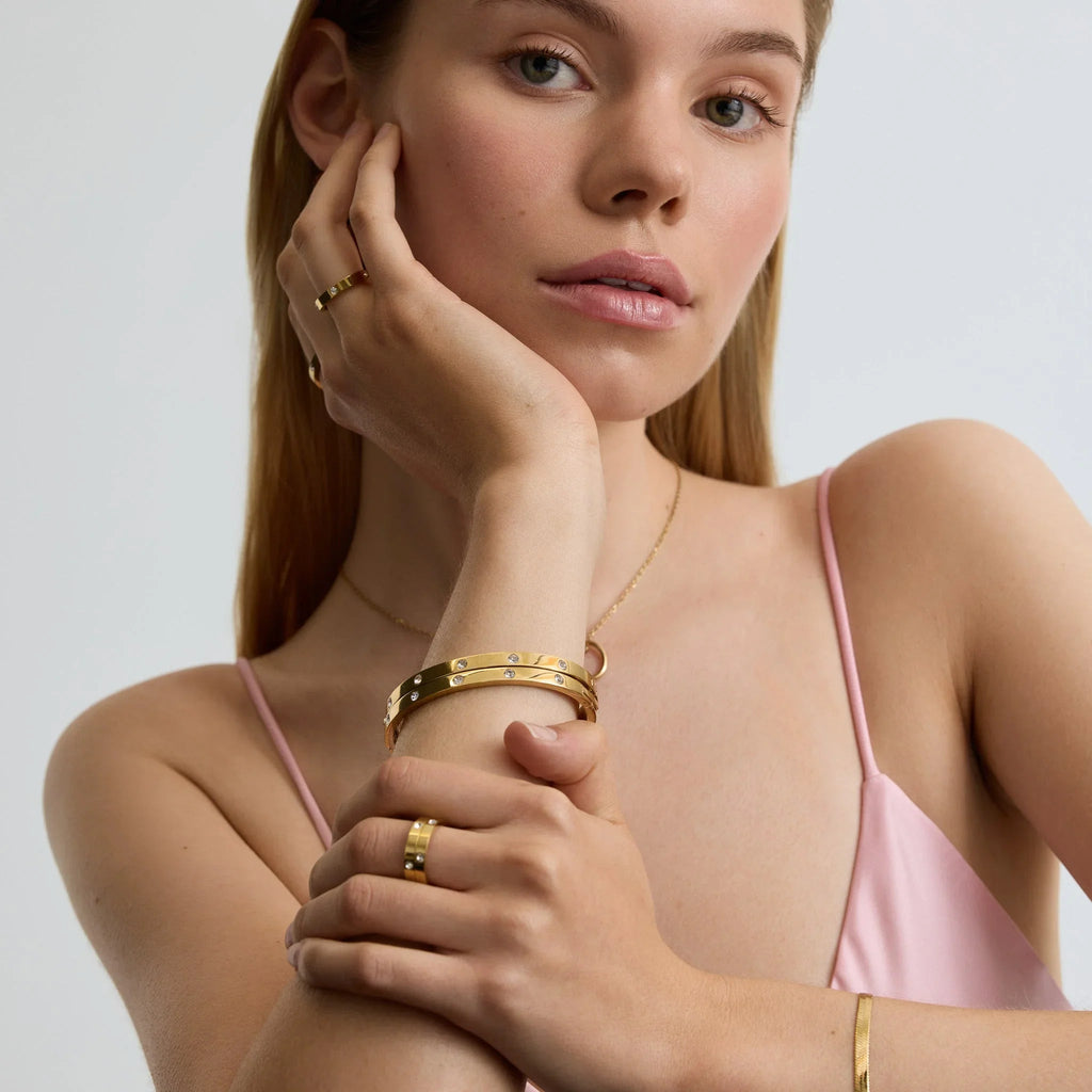 Woman wearing elegant gold eternity classic bangle bracelets and rings with diamond accents on arm and fingers