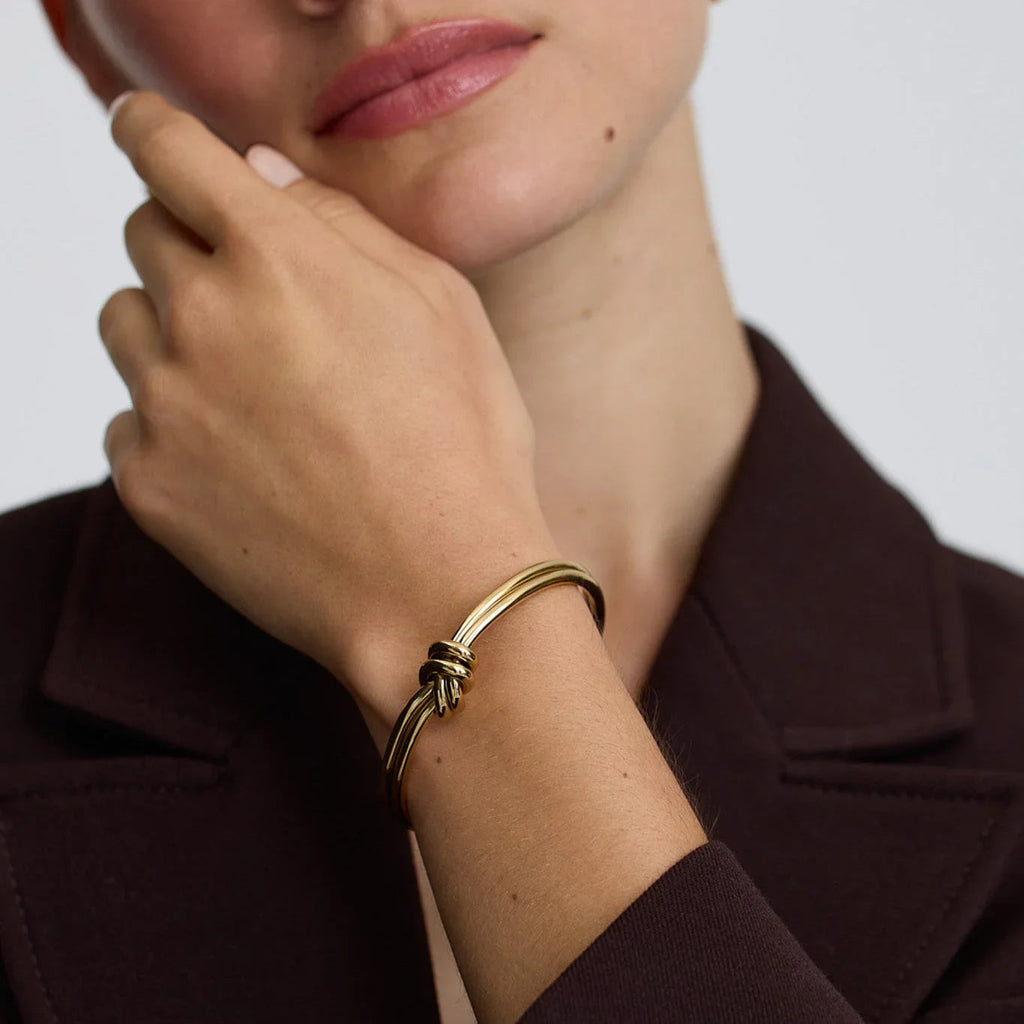 Close-up of woman wearing a gold knot bangle bracelet with a dark brown blazer