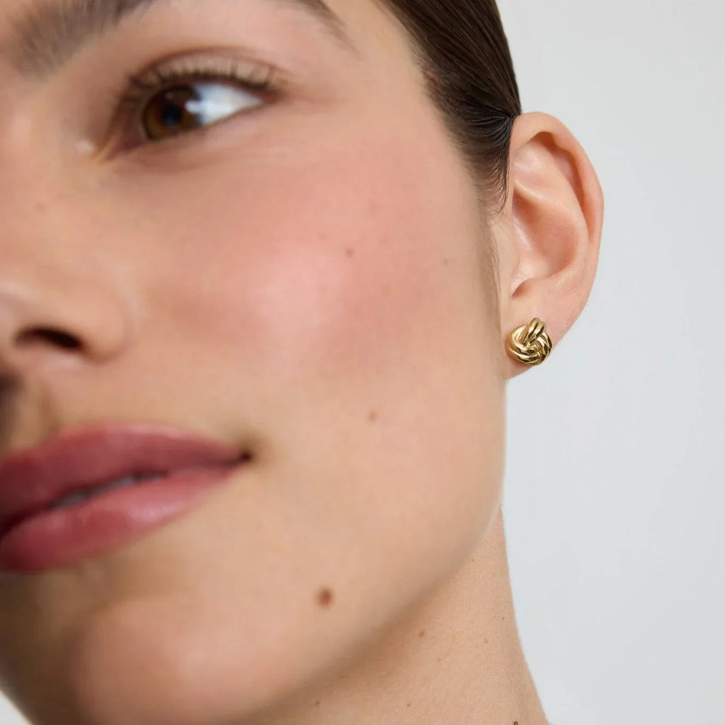 Close-up of woman wearing elegant gold knot stud earrings on white background