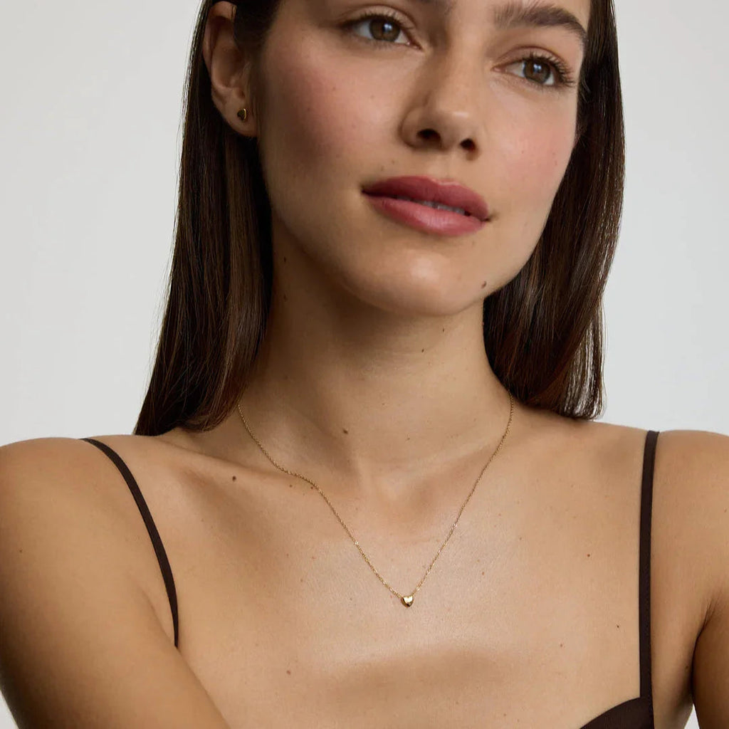 Close-up of woman wearing delicate gold heart pendant necklace with matching heart stud earrings