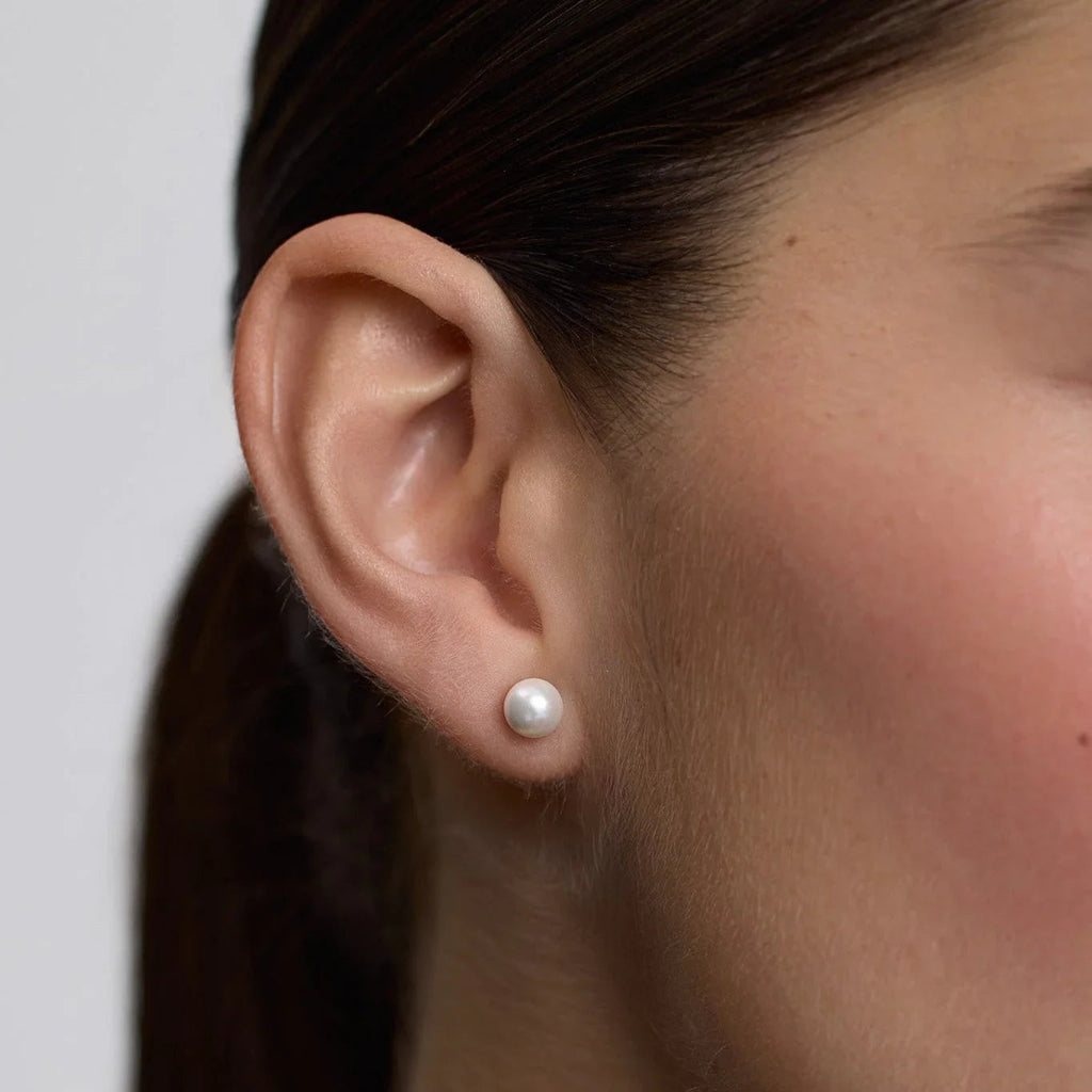 Close-up of a woman's ear wearing a single medium-sized white pearl stud earring