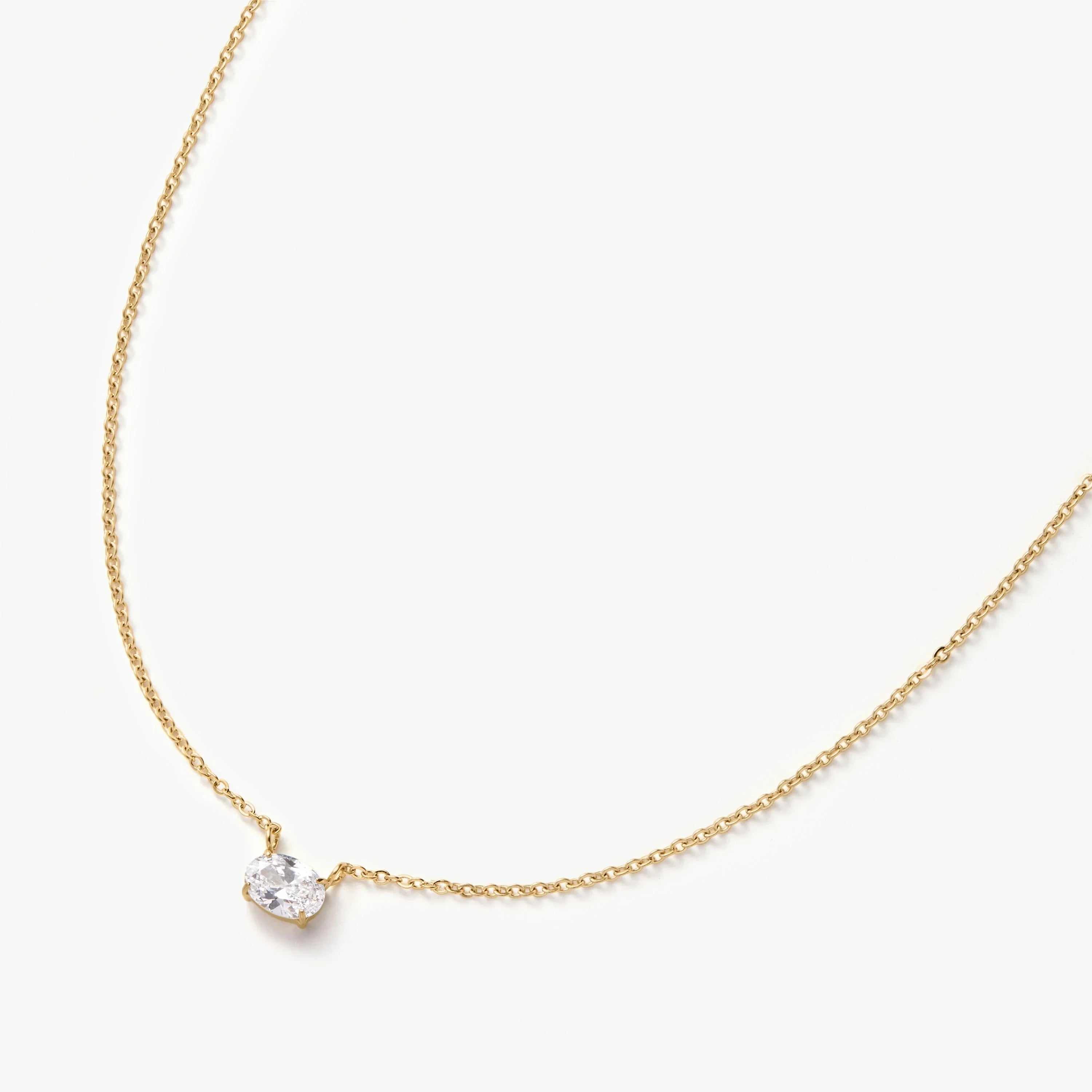 Delicate gold chain necklace with a single oval clear gemstone pendant on white background