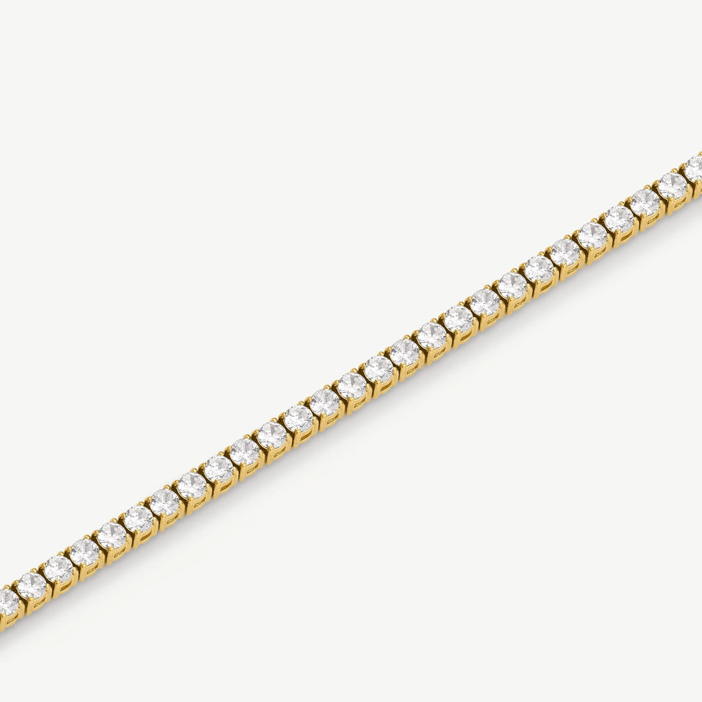 Close-up of gold tennis bracelet with round clear gemstones on white background