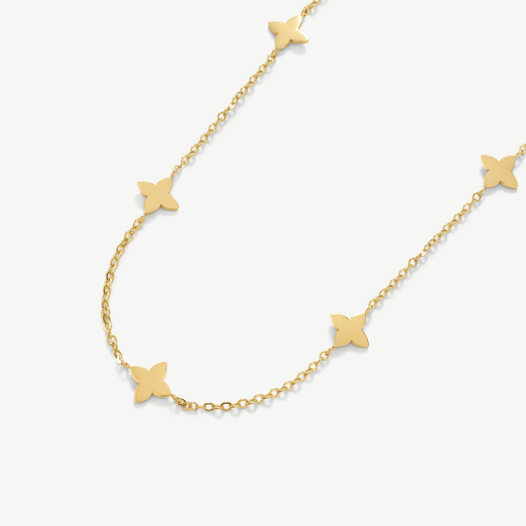 Gold chain necklace with four-petal flower charms on a white background