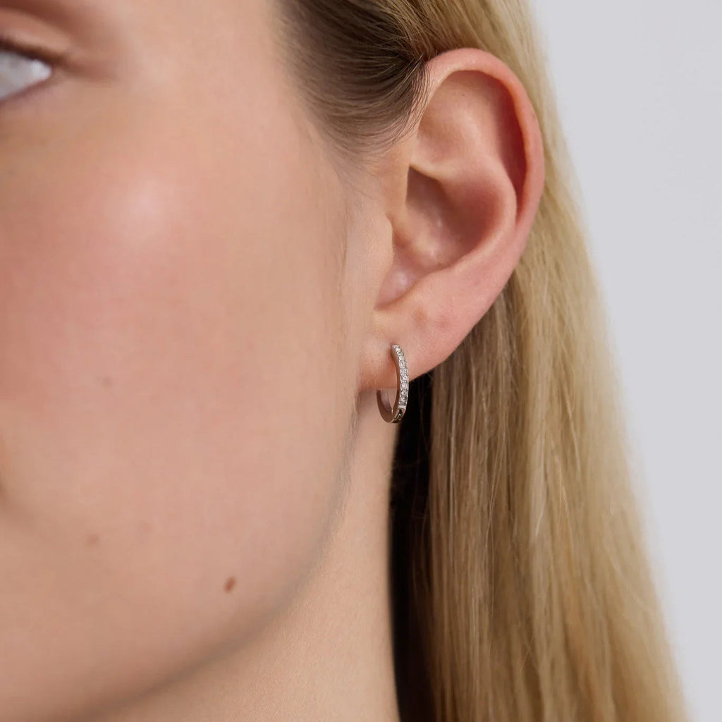 Close-up of a woman's ear wearing a small silver hoop earring with embedded clear crystals