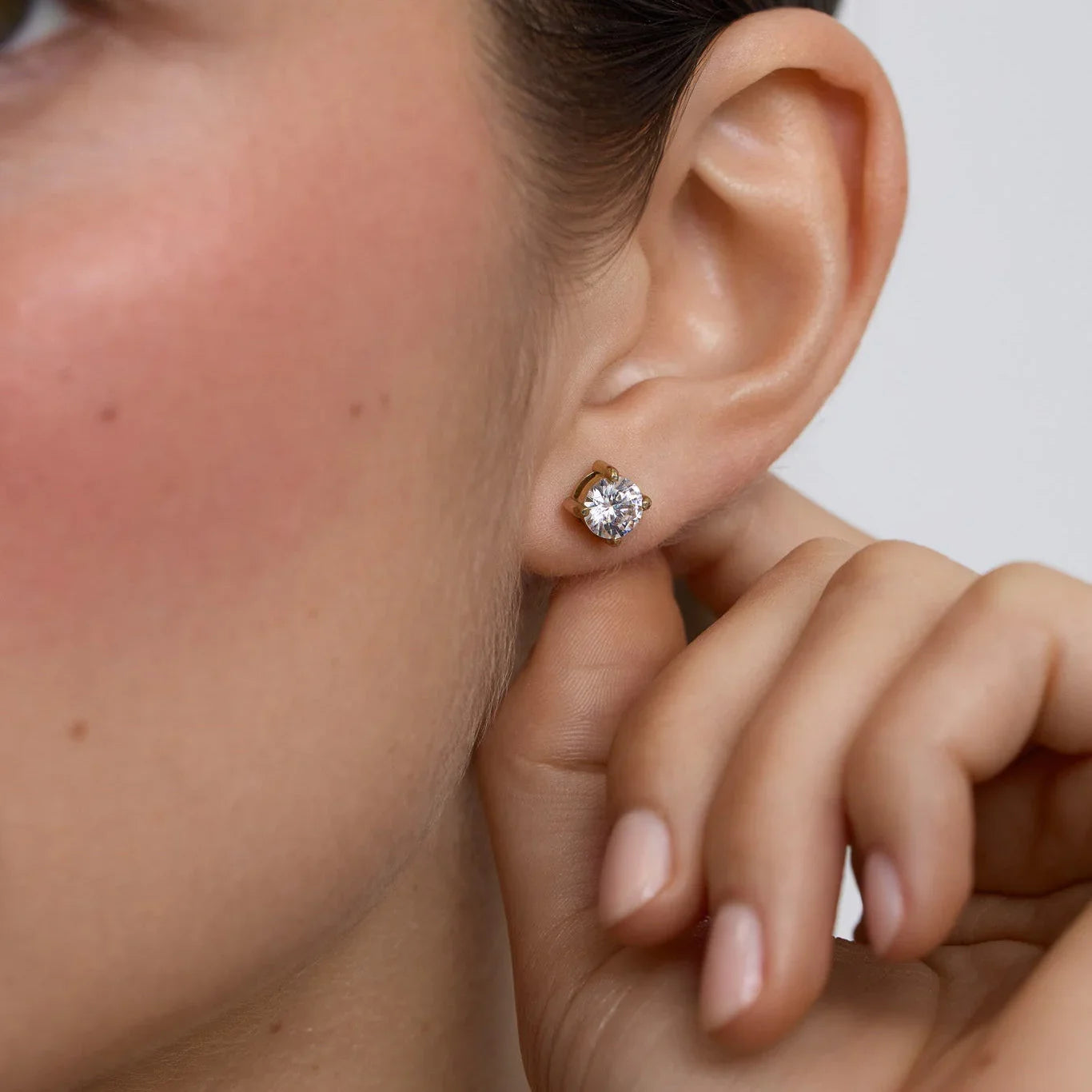 Close-up of a woman's ear wearing a gold stud earring with a sparkling clear gemstone