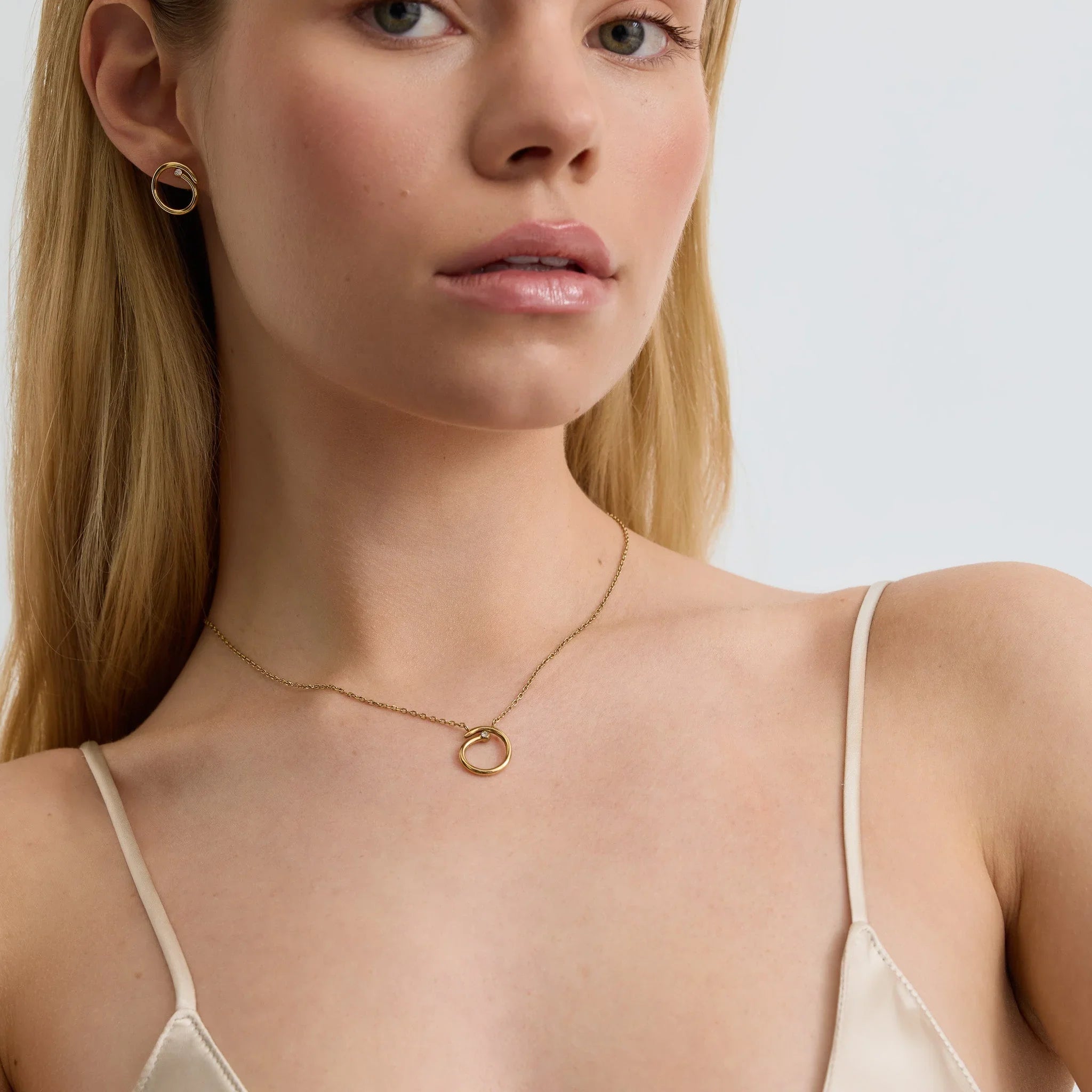 Close-up of woman wearing gold circle pendant necklace and matching gold hoop earrings with pearl detail