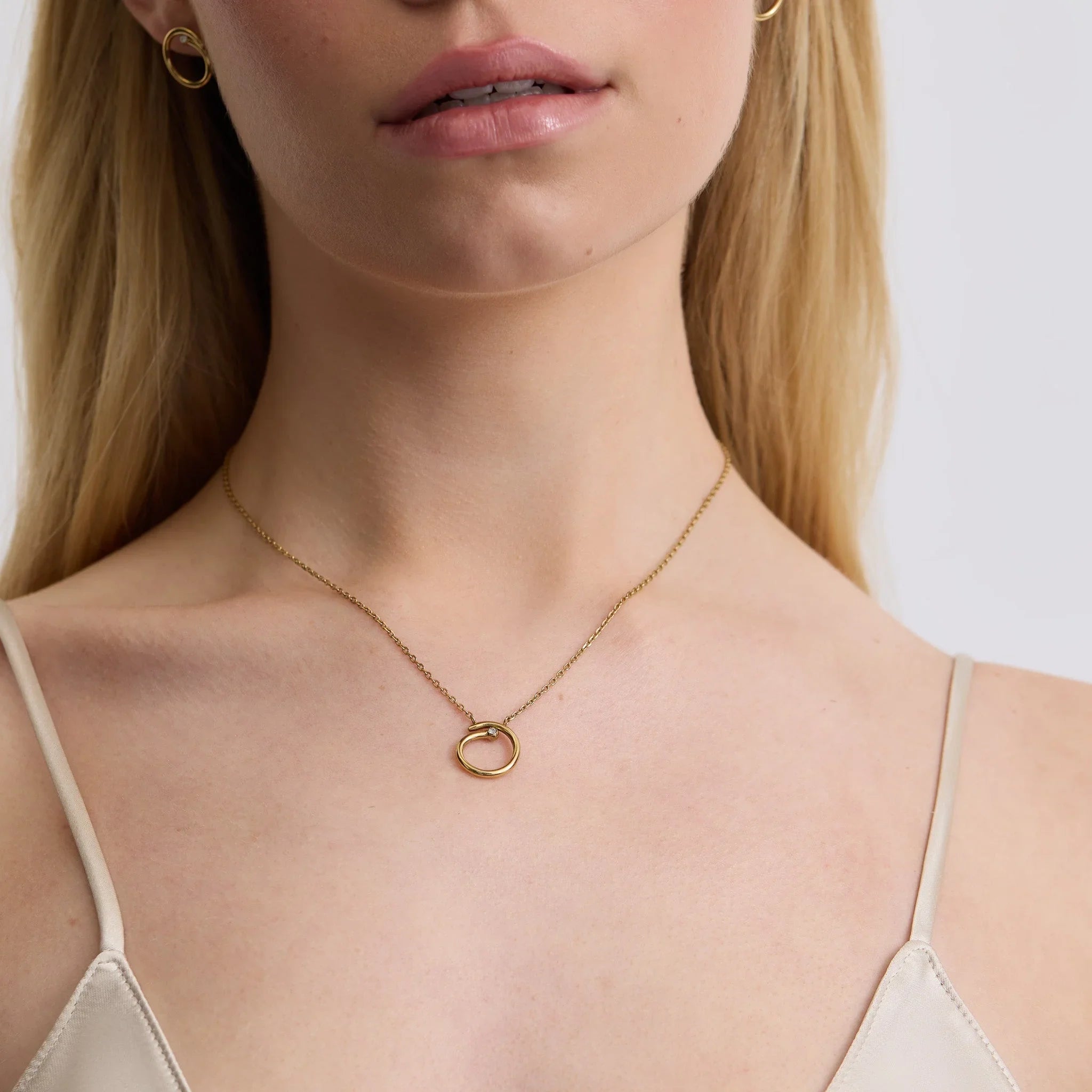 Close-up of a woman wearing a delicate gold circular pendant necklace and small gold hoop earrings