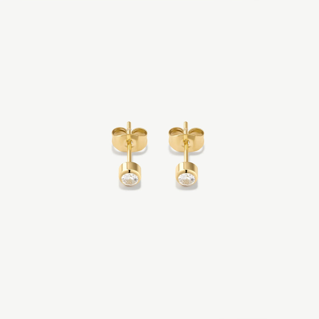 Pair of small gold stud earrings with bezel-set clear round gemstones on white background