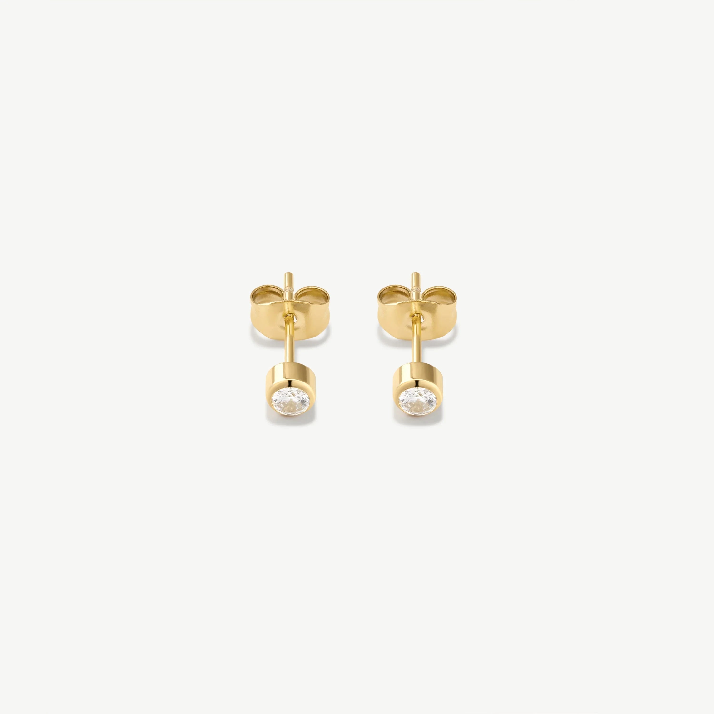 Pair of small gold stud earrings with bezel-set clear round gemstones on white background